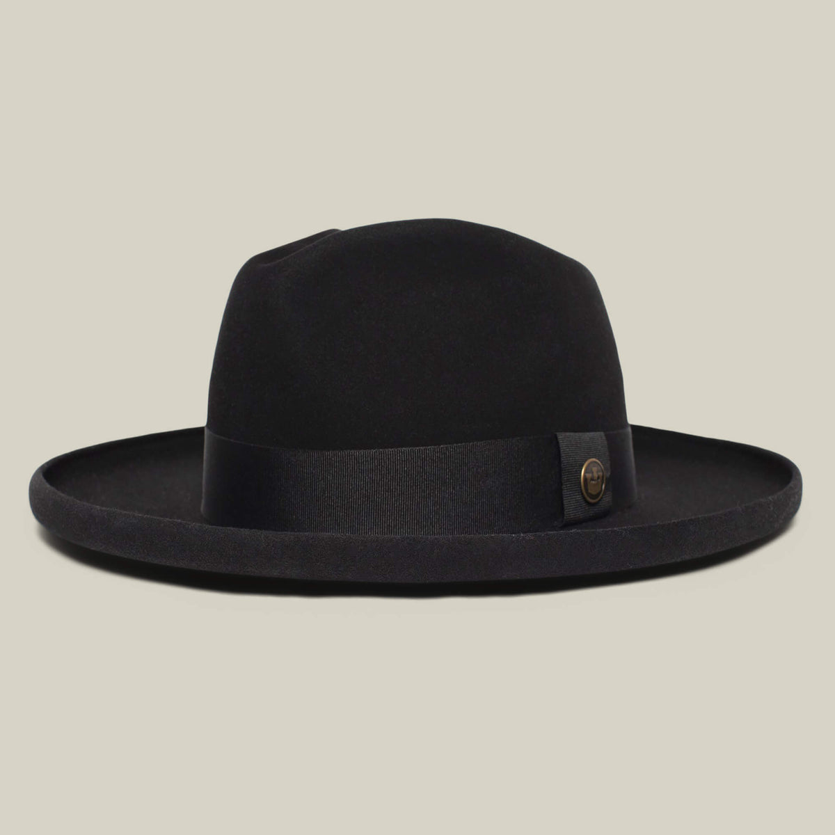 The Goorin Bros. Colonel Pierce is a black wide-brimmed fedora with a teardrop crown, black ribbon, and round metal emblem on the side, showcased against a plain beige background.