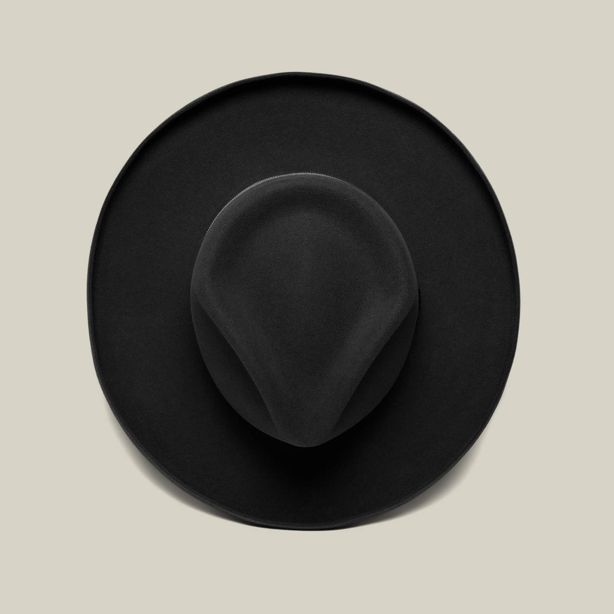 The Colonel Pierce by Goorin Bros., featuring a black teardrop crown and pencil curl brim, is photographed from above on a plain beige background.