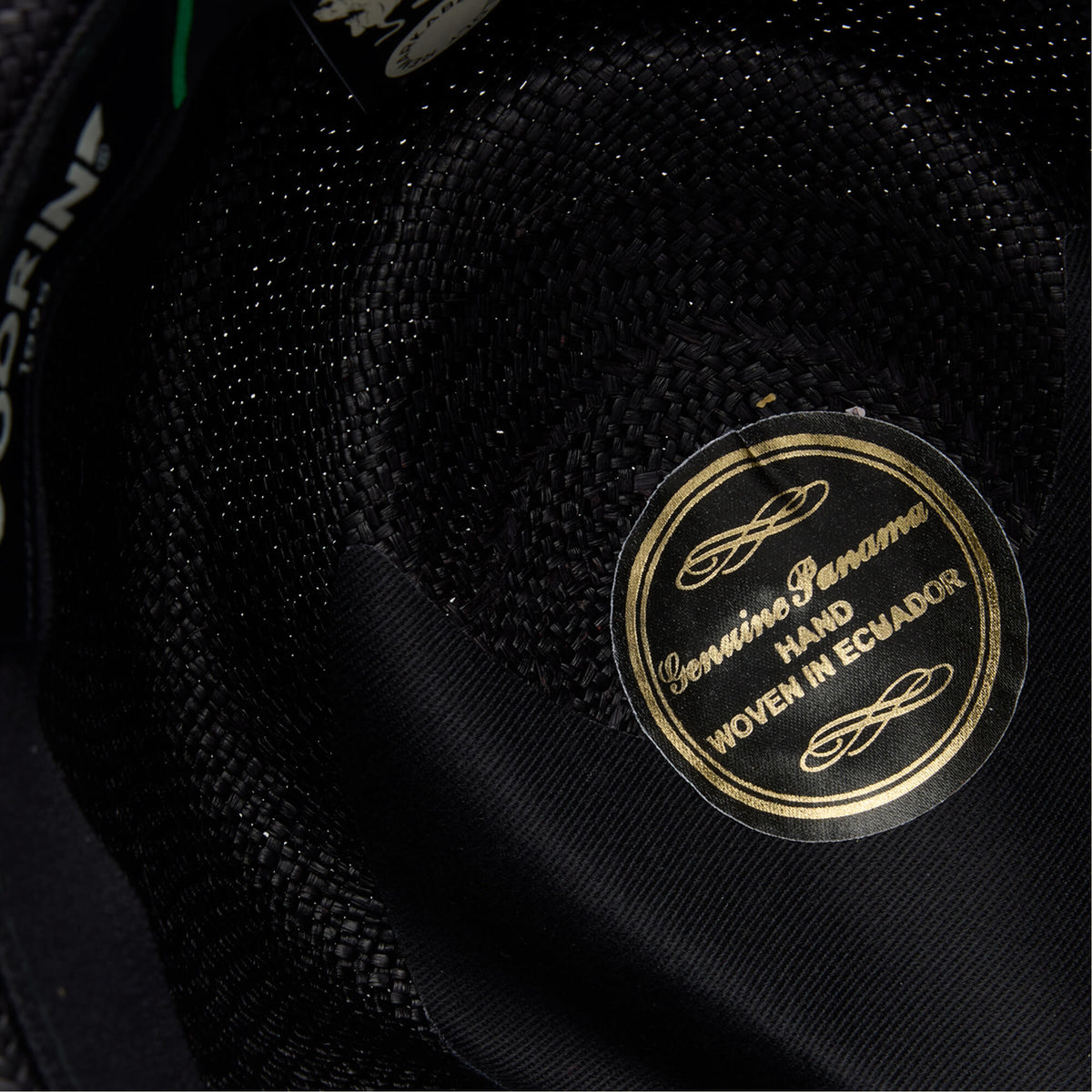 Close-up of the inside of a John Sr. black toquilla teardrop fedora by Goorin Bros., featuring a gold label reading Genuine Panama Hand Woven in Ecuador and offering 50 UPF sun protection.