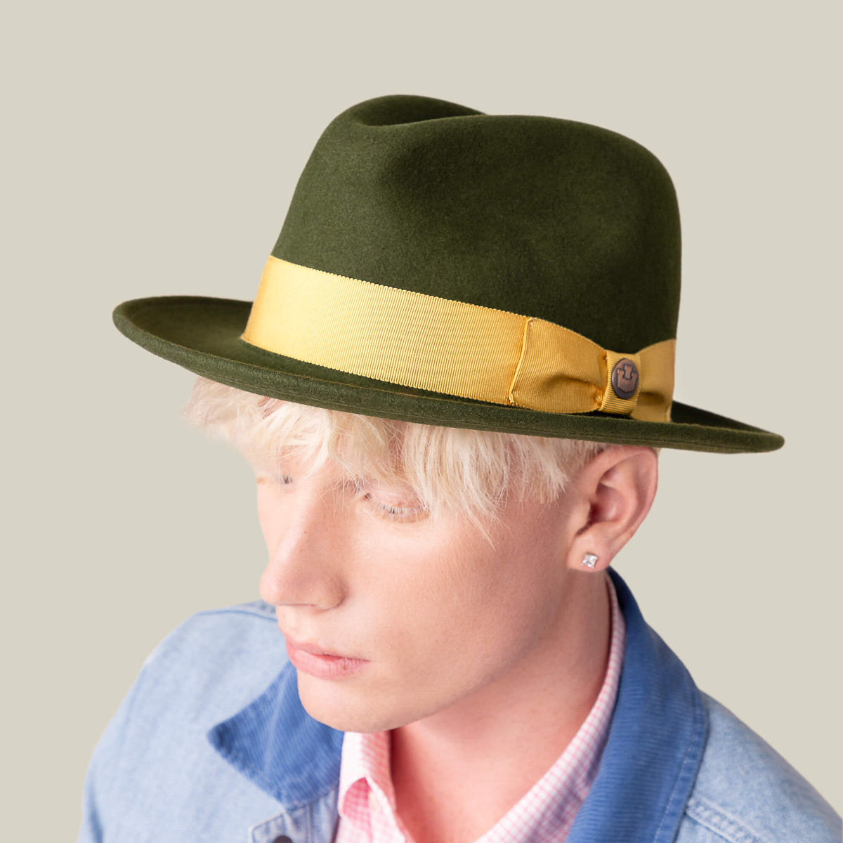 A person with blond hair wears Goorin Bros.' Dean the Butcher fedora—an American-made hat with a yellow grosgrain band—paired with a light pink shirt and light blue jacket, set against a plain background.