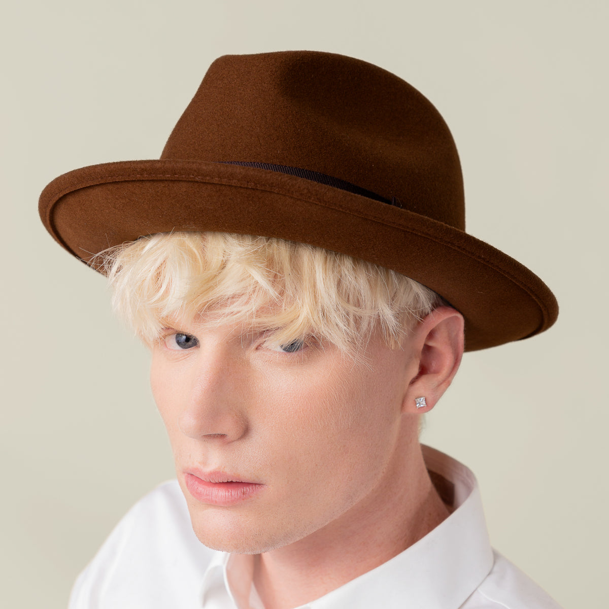 A person with short blond hair wears Goorin Bros.' American-made Dean the Butcher fedora with grosgrain hatband, a white shirt, and a stud earring, looking at the camera against a neutral background.