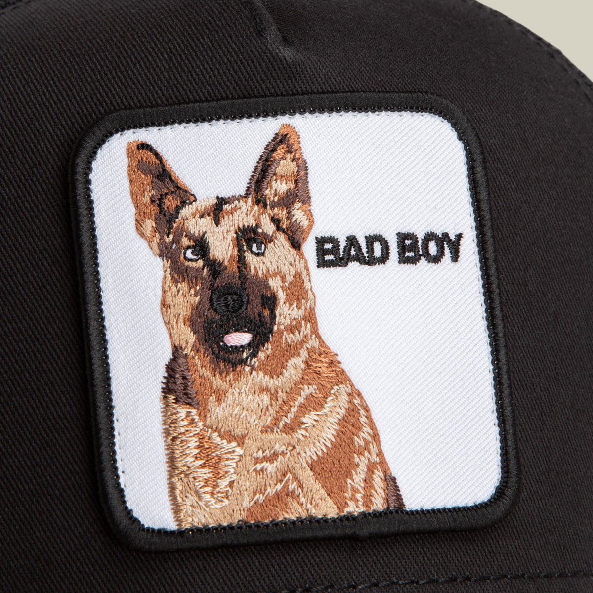 The Bad Boy by Goorin Bros is a black trucker cap featuring an embroidered German Shepherd patch with "Bad Boy" text on a white background.