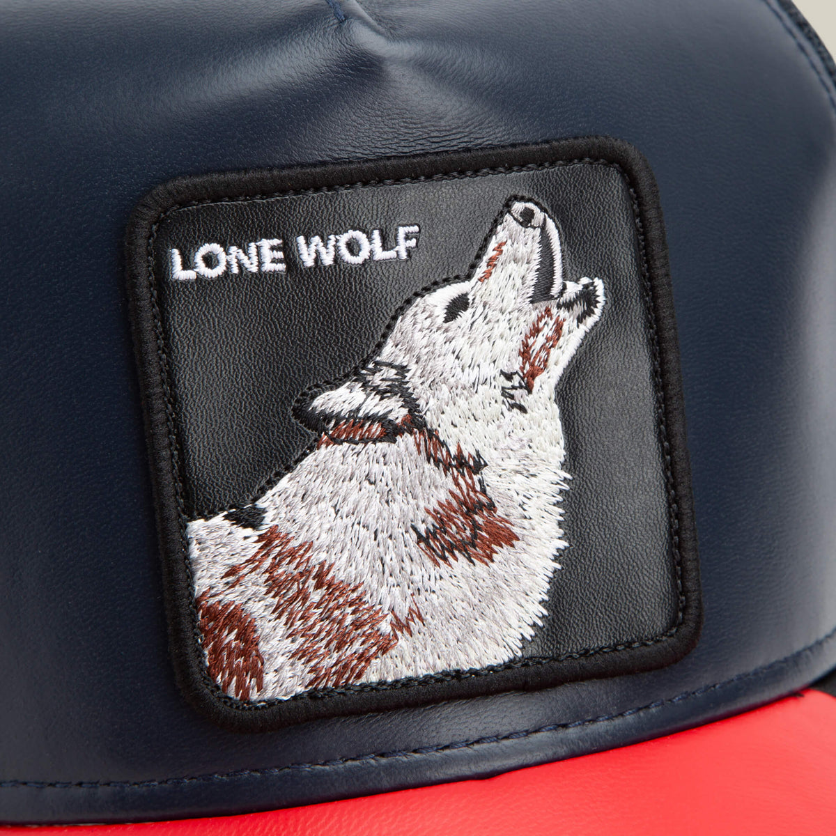 A close-up of The Farm's Shleather Wolf cap in navy blue and red, featuring a howling wolf patch with "LONE WOLF" text—ideal for trendy, statement style.