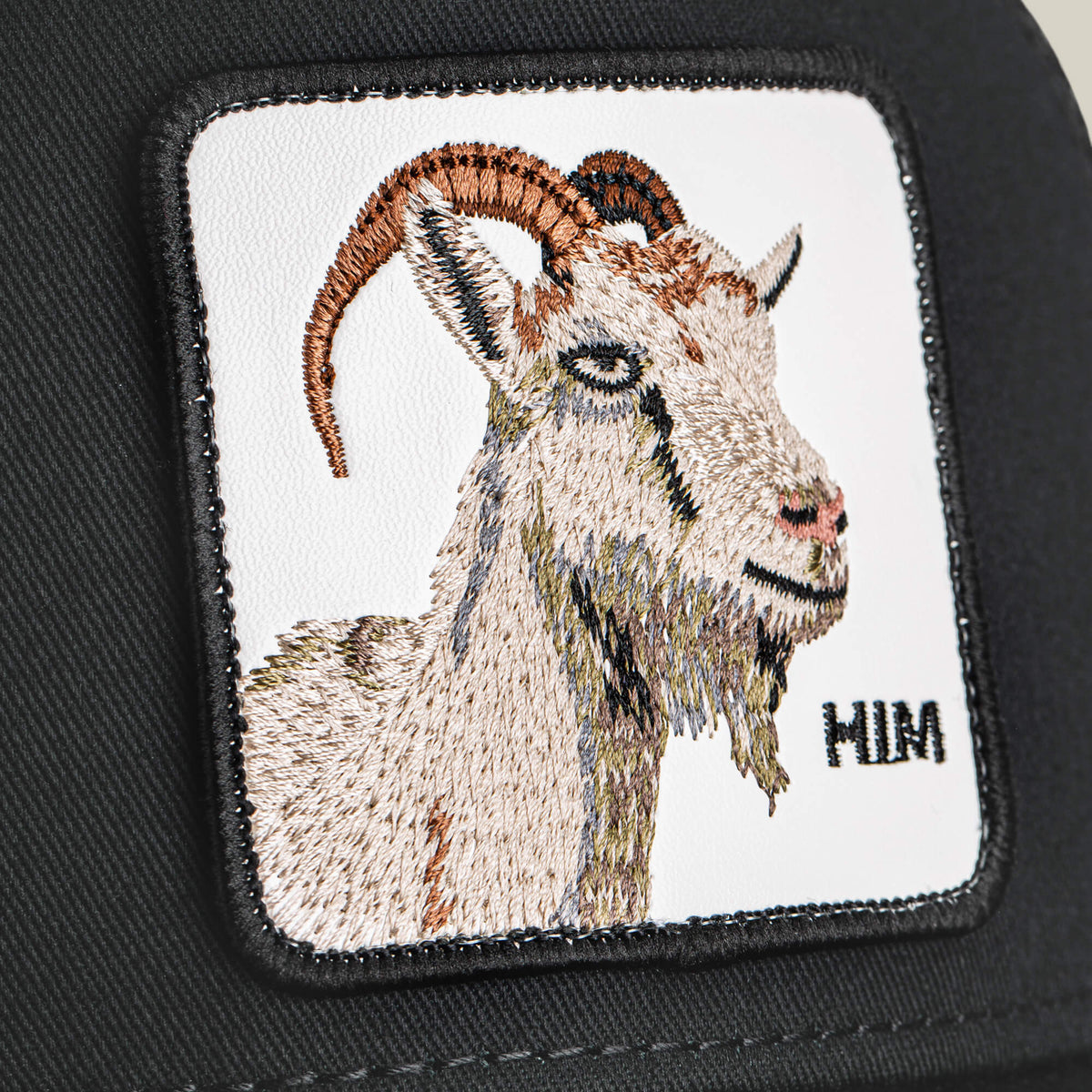 Embroidered patch featuring a GOAT's head with curved horns on black fabric, detailed stitching, and "MIM" text in the lower right. Product: Him Trucker by Goorin Bros.
