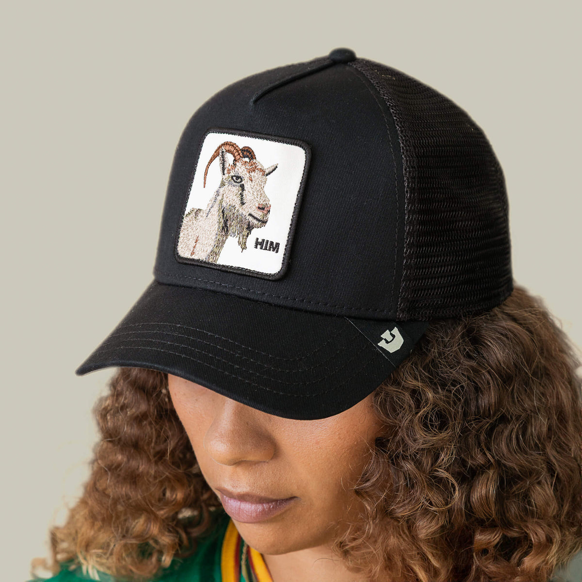A person is wearing the Him Trucker by Goorin Bros., a black mesh baseball cap featuring a stitched patch with a goat and the word "HIM.