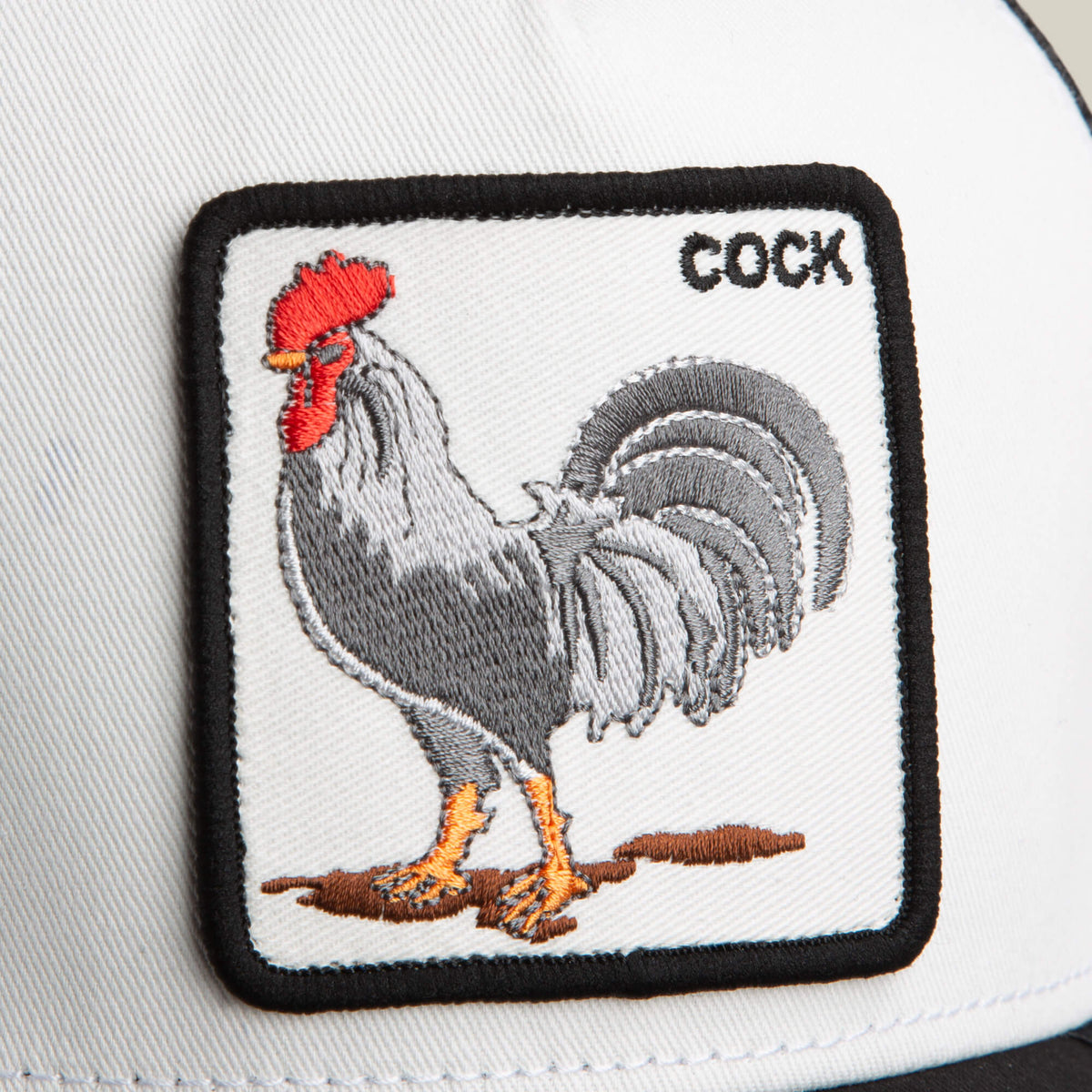 A white Rooster Trucker hat by Goorin Bros., featuring a stitched rooster patch and the word "COCK" in the top right corner.