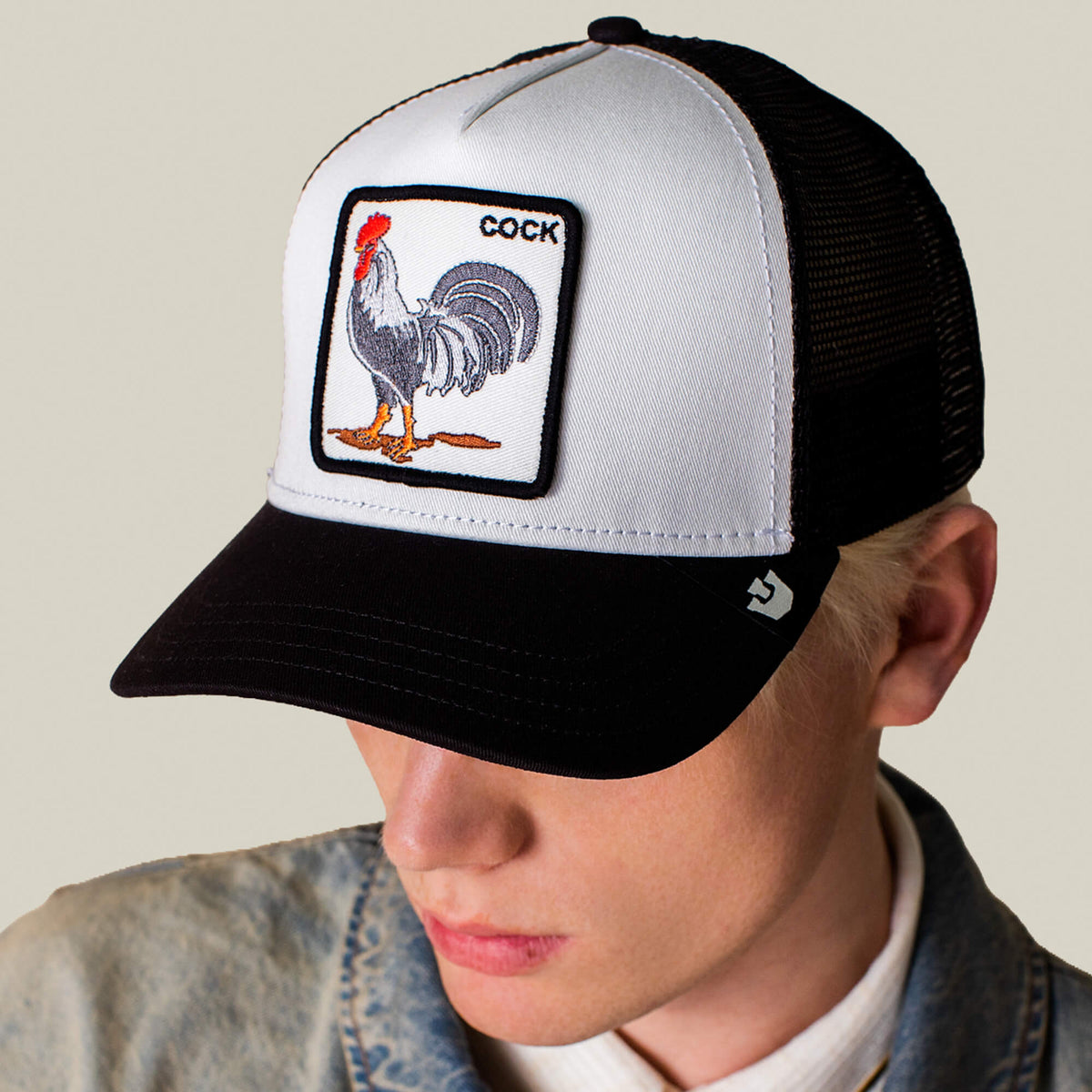 A person wearing a Goorin Bros. Rooster Trucker hat in black and white, featuring a bold rooster patch labeled "COCK" on the front.