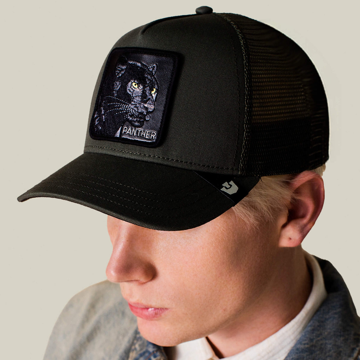A person wears the Goorin Bros. Panther Trucker—a black mesh cap with a panther patch and PANTHER text—paired with a light button-up shirt and jacket.