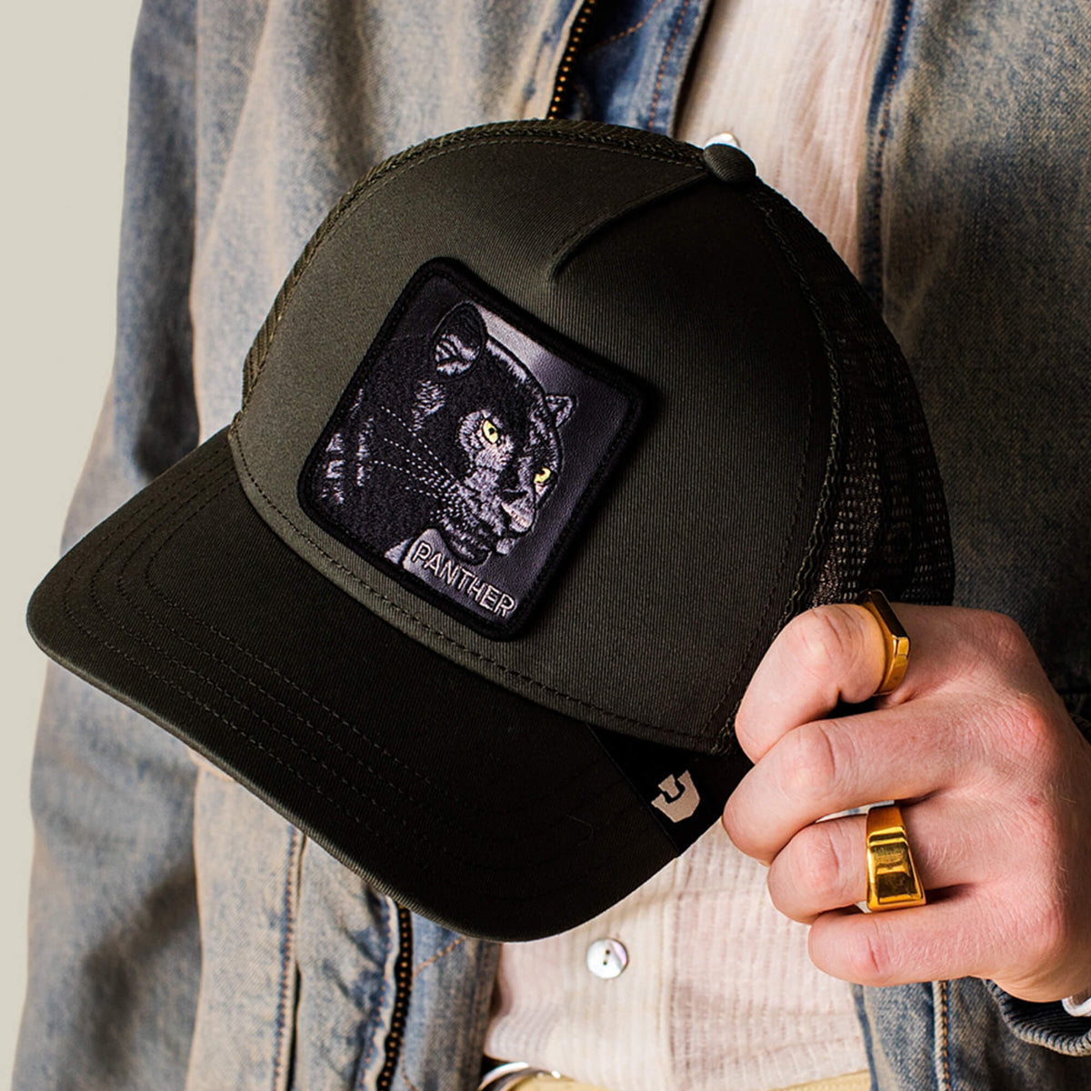 A person holds the Panther Trucker hat by Goorin Bros.—a black mesh trucker style featuring a front patch with an embroidered black panther and the word PANTHER.
