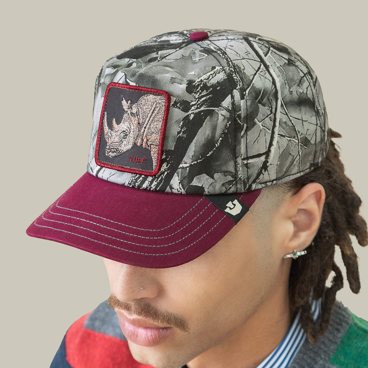 A person wears the Goorin Bros. Tuff Camo low crown baseball cap with a rhino patch and "Tuff" text, paired with a multicolored shirt, set against a plain background.