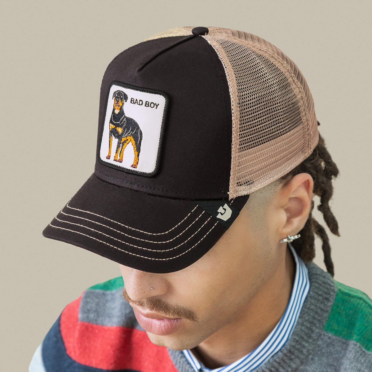A person wears the Goorin Bros. Bad Boy Trucker, a black and tan mesh hat with a dog patch on the front—an edgy accessory that makes a bold style statement.
