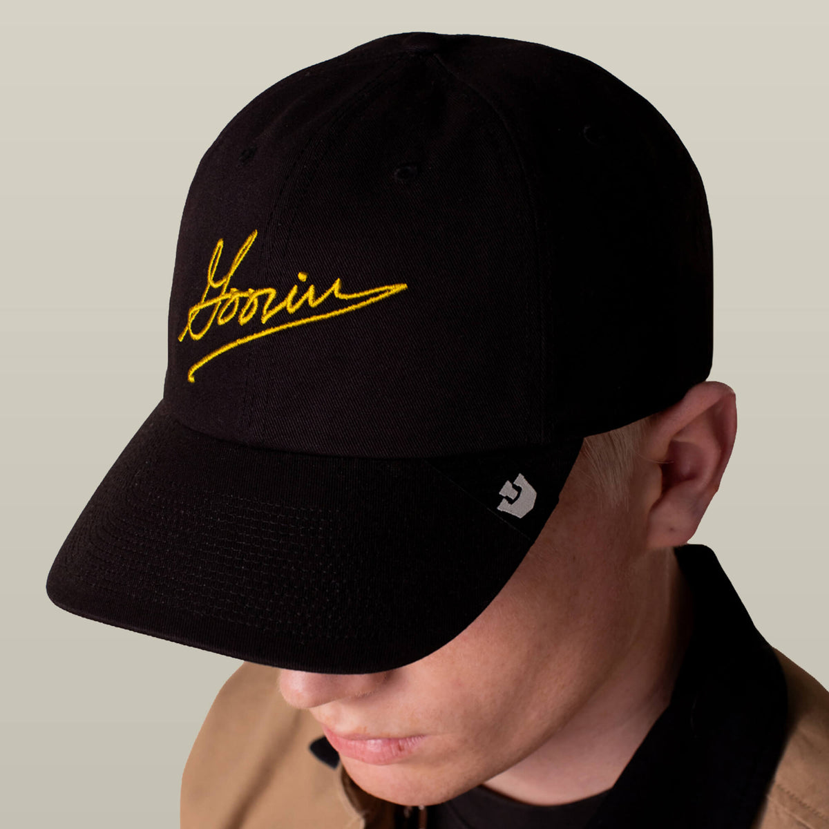 A person wearing the Goorin Bros. Goorin Script Papa cap in black, featuring yellow script and a small white logo on the brim, looks down.