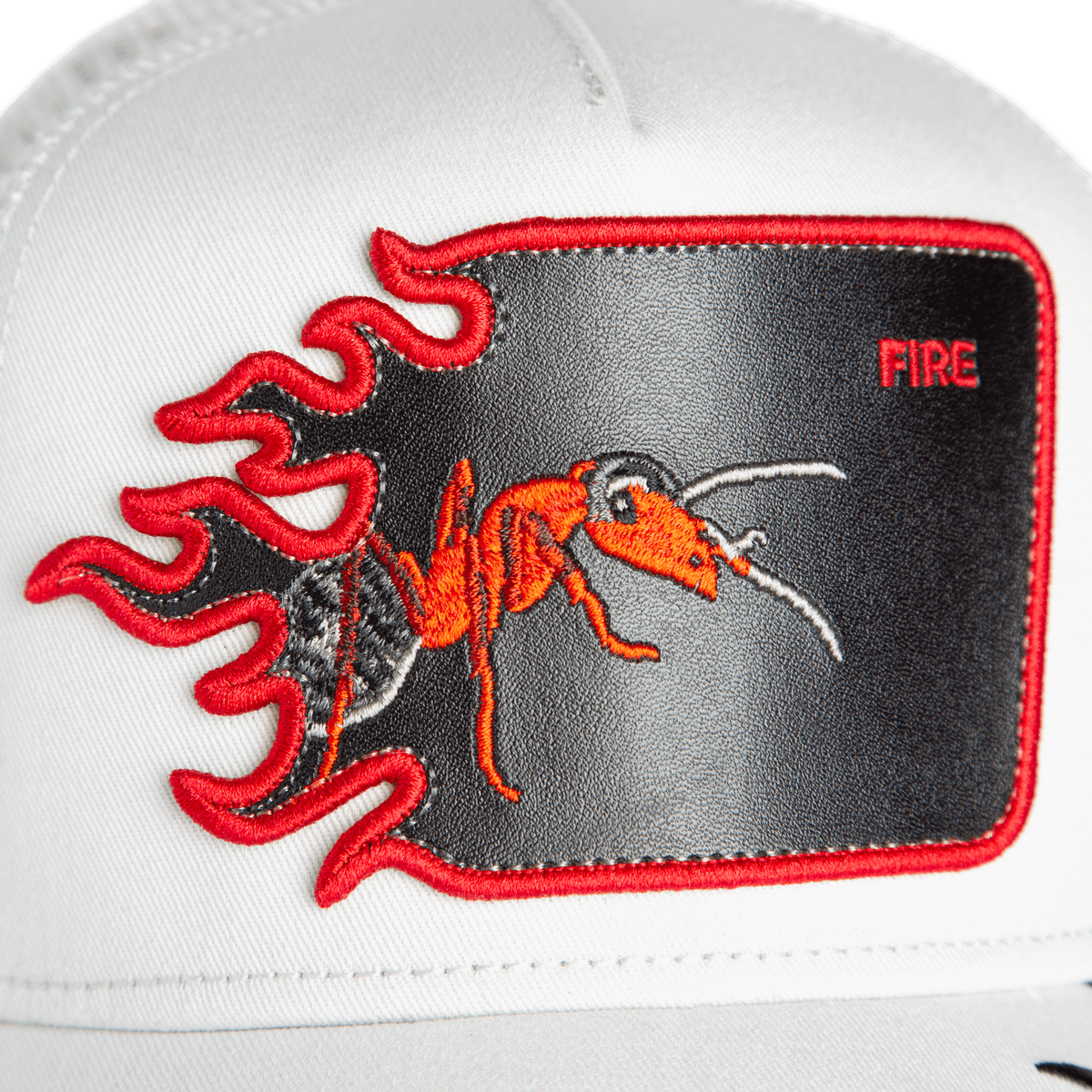 The Goorin Bros. Fire Flames trucker hat is white with a red ant patch, embroidered fire flames, and the word "FIRE" in the top right corner.
