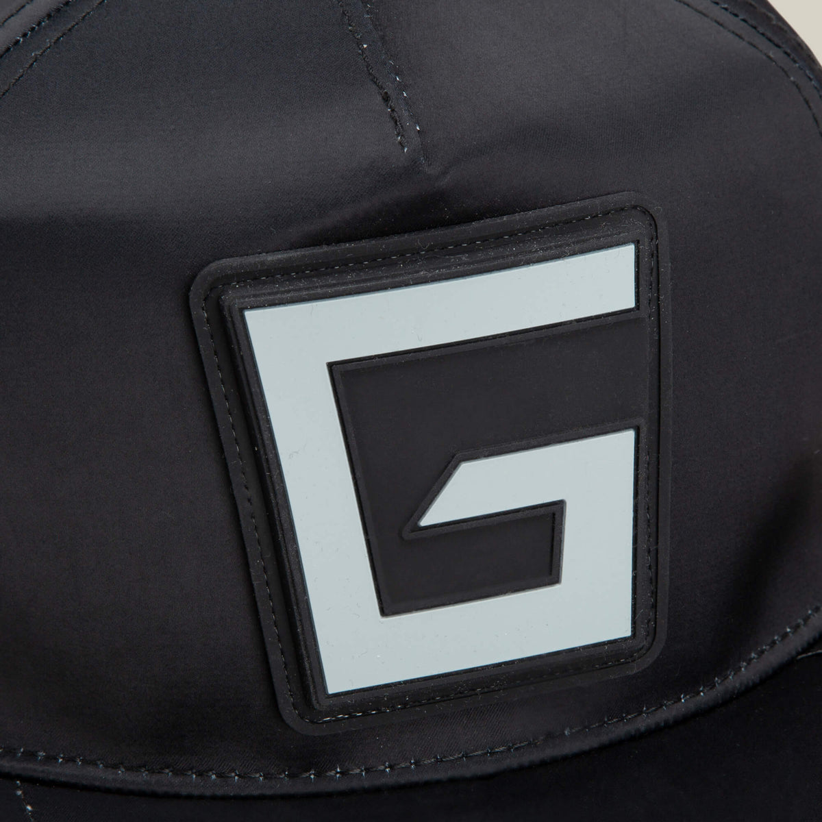 Close-up of the Goorin Bros. Pole Position - Road Kill racing cap in black fabric, featuring a prominent square patch with a stylized black and white G logo on the front and subtle chrome satin stripes for a sleek, modern finish.