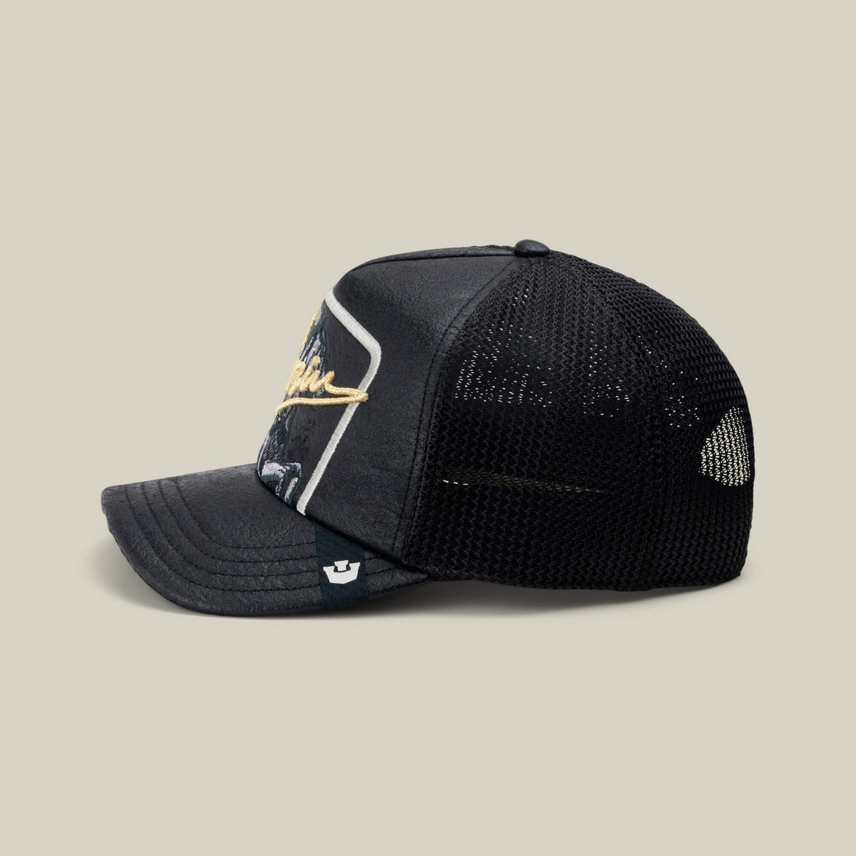 The NeoBrand STALLION by Goorin Bros. is a black mesh trucker hat with a curved brim and monochrome embroidery on the front, shown in side profile against a plain background. Pair with black sneakers for a sleek, coordinated style.