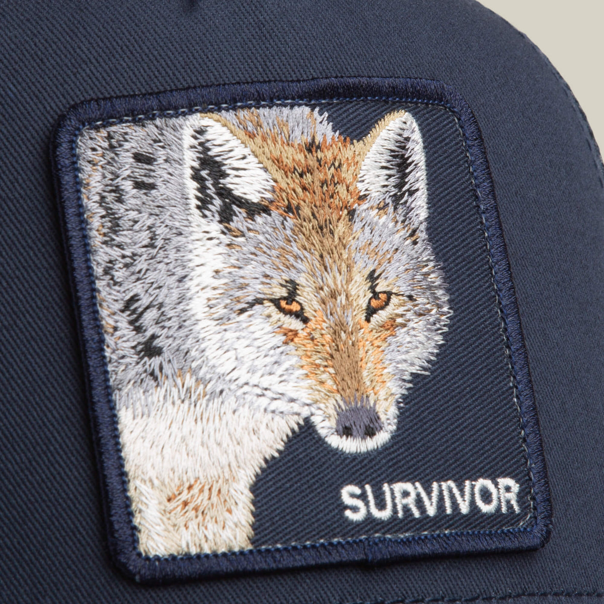 The Mirage Survivor by Goorin Bros. is a navy blue trucker cap featuring an embroidered coyote head patch and the word "SURVIVOR.