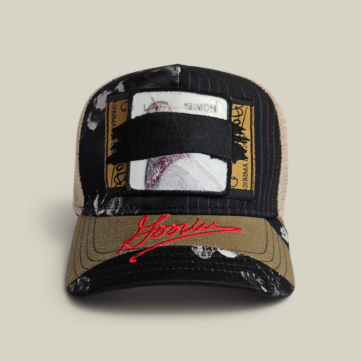 The Goorin Bros. Goorin Rework Trucker in VOID features a mesh back, ID card patch front, black strap detail, red embroidery, and paint splatter accents—available as a limited edition.