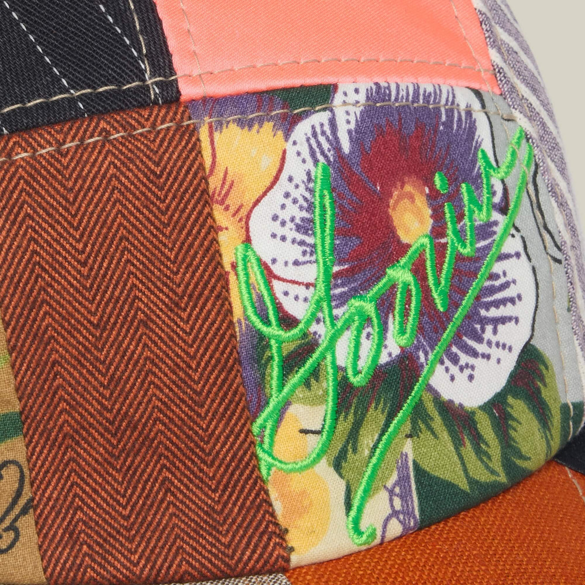 A close-up of the Goorin Bros. Goorin Rework Camper, a limited edition patchwork fabric hat with multicolored patterns, a flower design, and neon green Goorin embroidery.