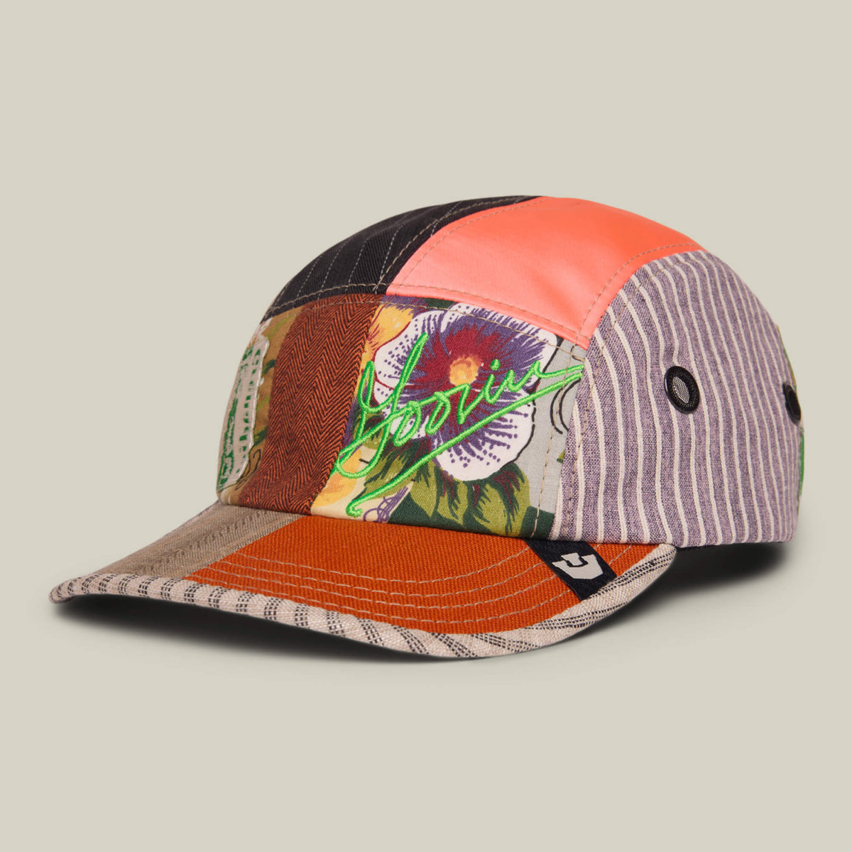 The Goorin Rework Camper by Goorin Bros. is a limited edition patchwork baseball cap featuring stripes, solids, and a floral graphic with neon green lettering on a neutral background. Made in the USA.