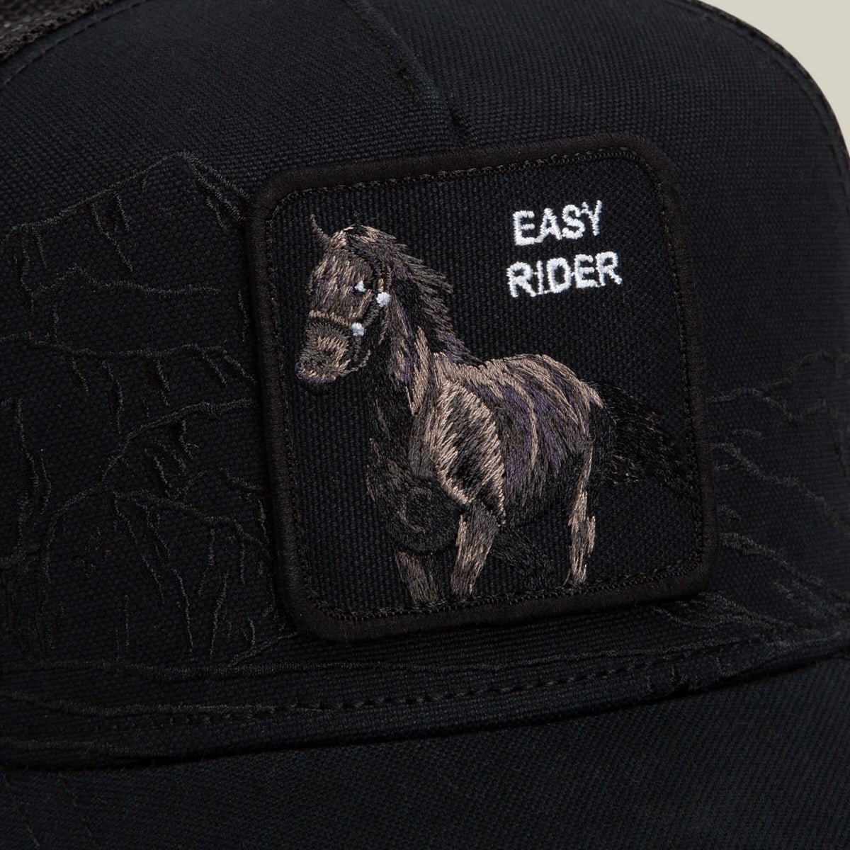 Goorin Bros. Badlands Stallion black cap featuring a patch with an embroidered horse and the words EASY RIDER in white lettering. Subtle mountain outlines appear in the background of the fabric.