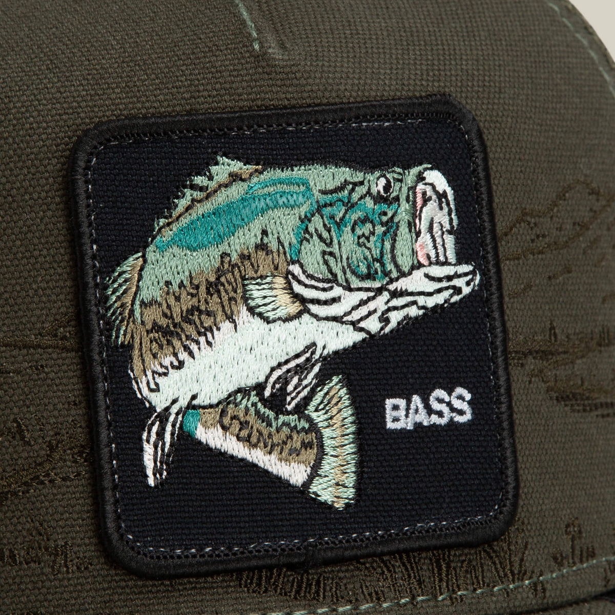 Close-up of the Goorin Bros. Badlands Bass cap in dark green, showcasing a stitched patch with an illustrated largemouth bass and the word "BASS" in white text.