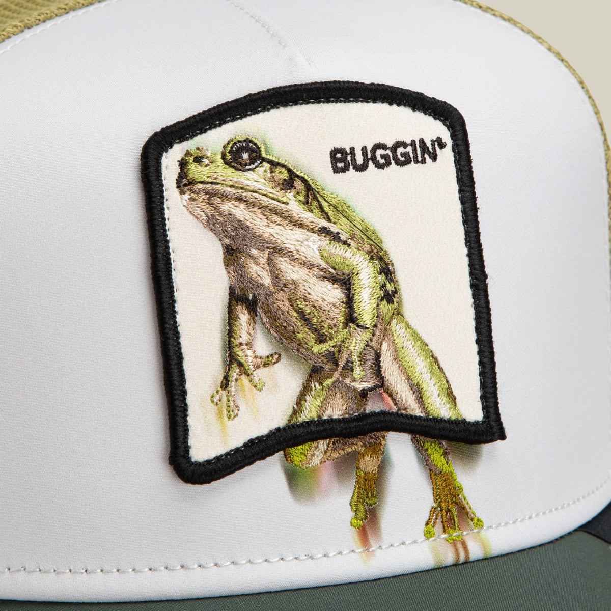 The Goorin Bros. Migration - Buggin' trucker hat features a white crown with black mesh back and a detailed embroidered green frog patch labeled "Buggin'" on the front.