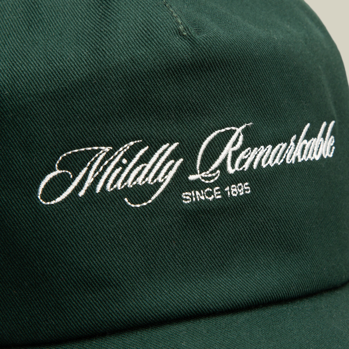 Close-up of the Goorin Bros. Mildly Remarkable Script dark green low pro fit cap featuring "Mildly Remarkable" and "SINCE 1895" embroidered in white script on the front, highlighting its classic embroidery.