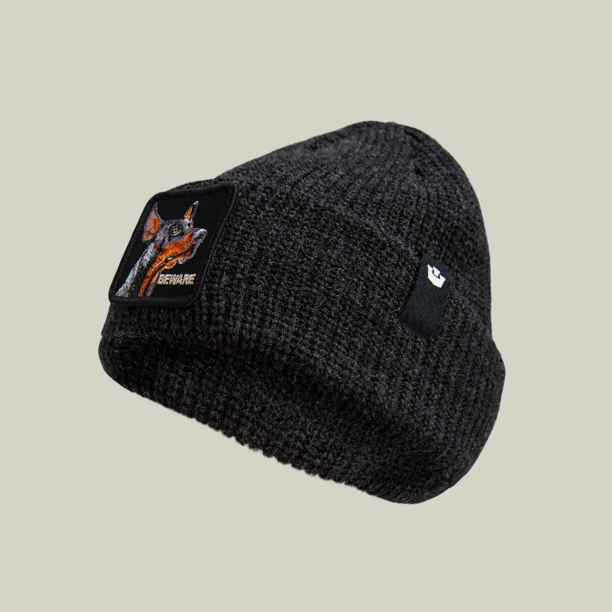 The Beware Beanie by Goorin Bros. is a dark gray heavyweight knit beanie featuring a fox patch with "BEWARE" and a small black rectangular label on the folded brim.