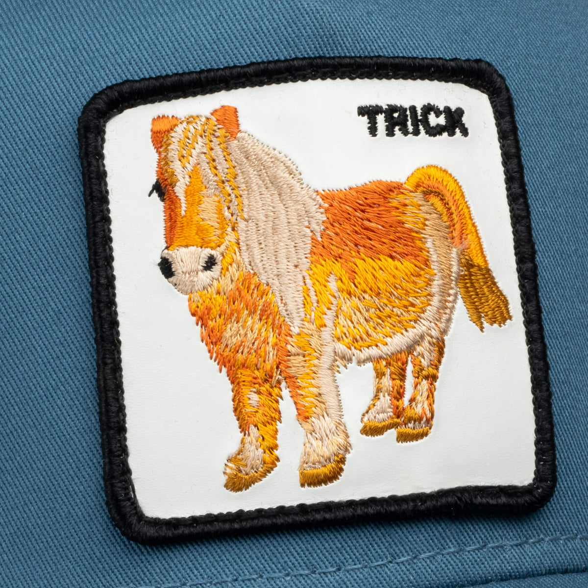 A rectangular embroidered patch from Goorin Bros. features a small orange and white pony and "TRICK" stitched in black on blue fabric. Product name: Dad and Pony Show (Kids).