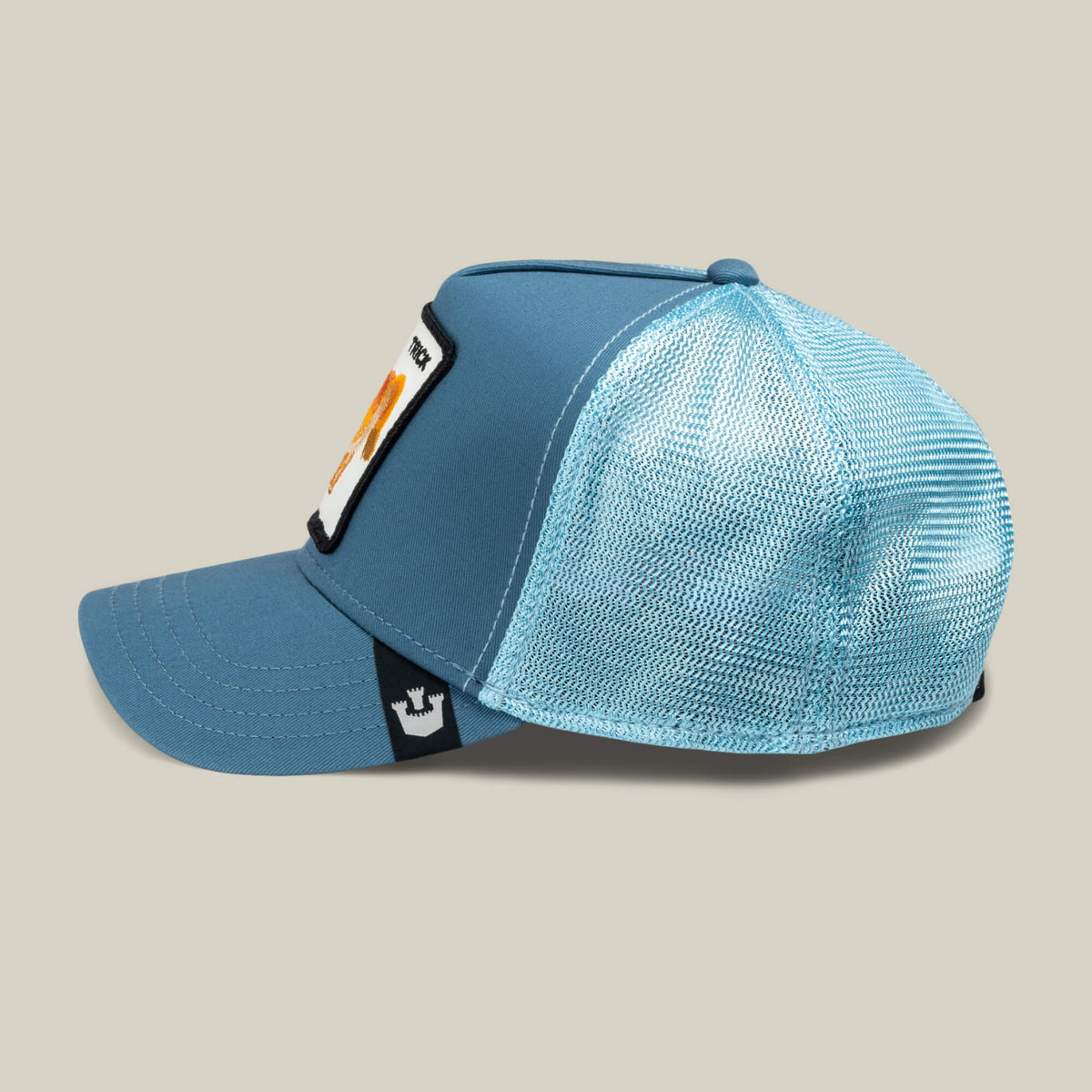 The Goorin Bros. Dad and Pony Show (Kids) is a blue trucker hat featuring a mesh back, fabric front panel, flat brim, and rectangular patch. Shown in profile against a plain beige background.