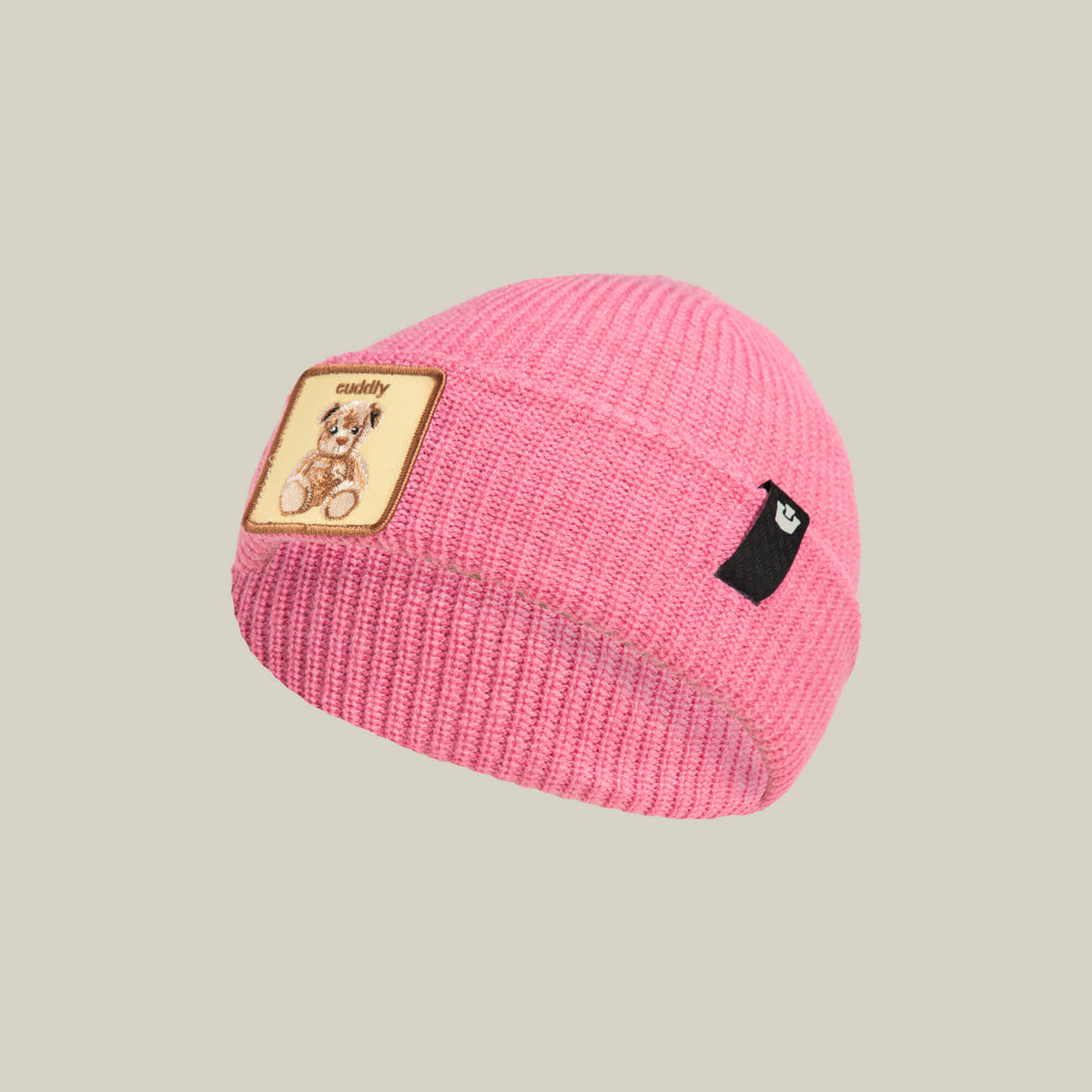 The Cuddly Beanie Mini by Goorin Bros. is a soft knit pink kids beanie featuring a teddy patch with a cute bear illustration and "cuddly" text, plus a small black side tag.