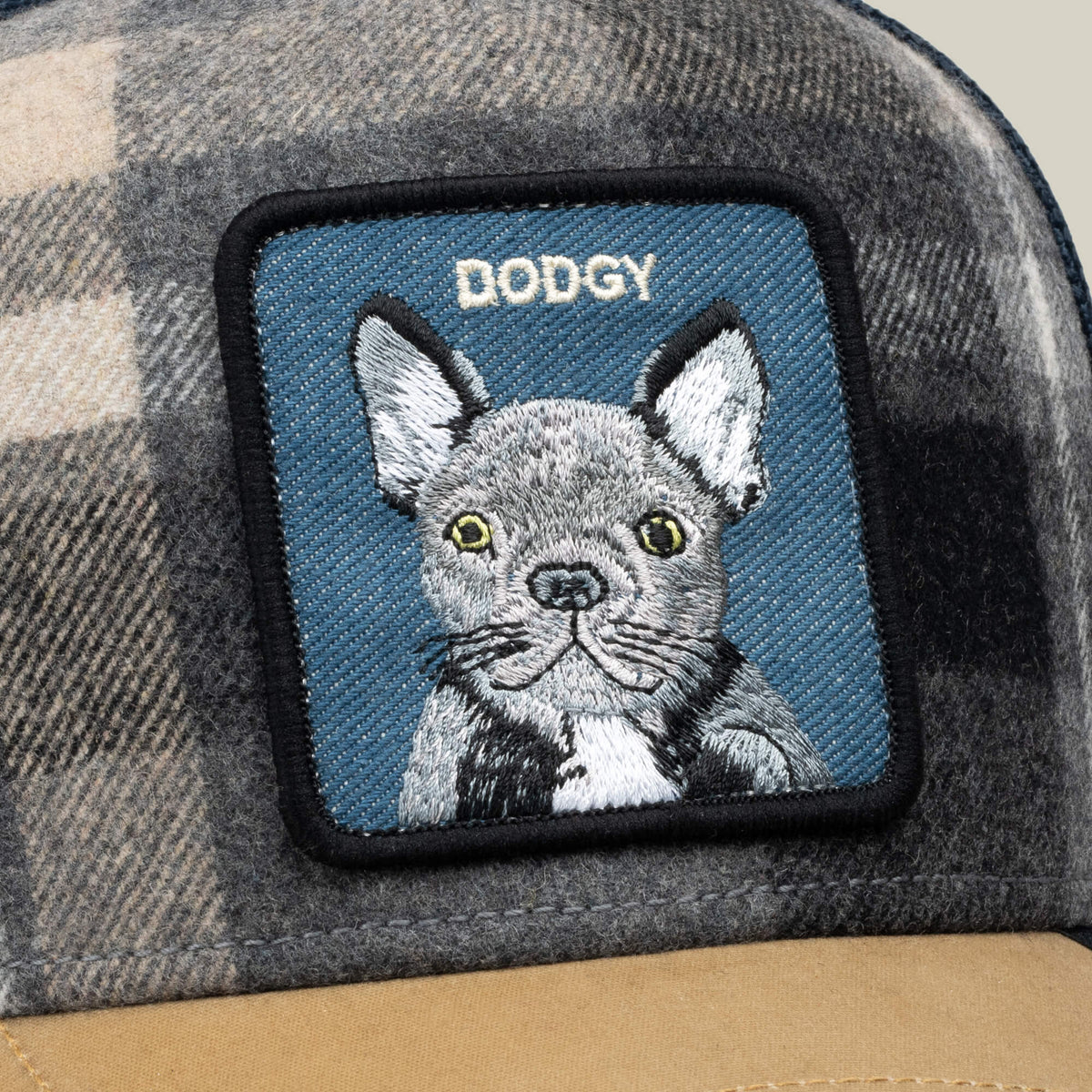 Close-up of the Brit Frenchie adjustable plaid cap by Goorin Bros., featuring a patch with an illustrated dog and the word “DODGY” above it. This stylish hat also has an embroidered mesh back for enhanced comfort and breathability.
