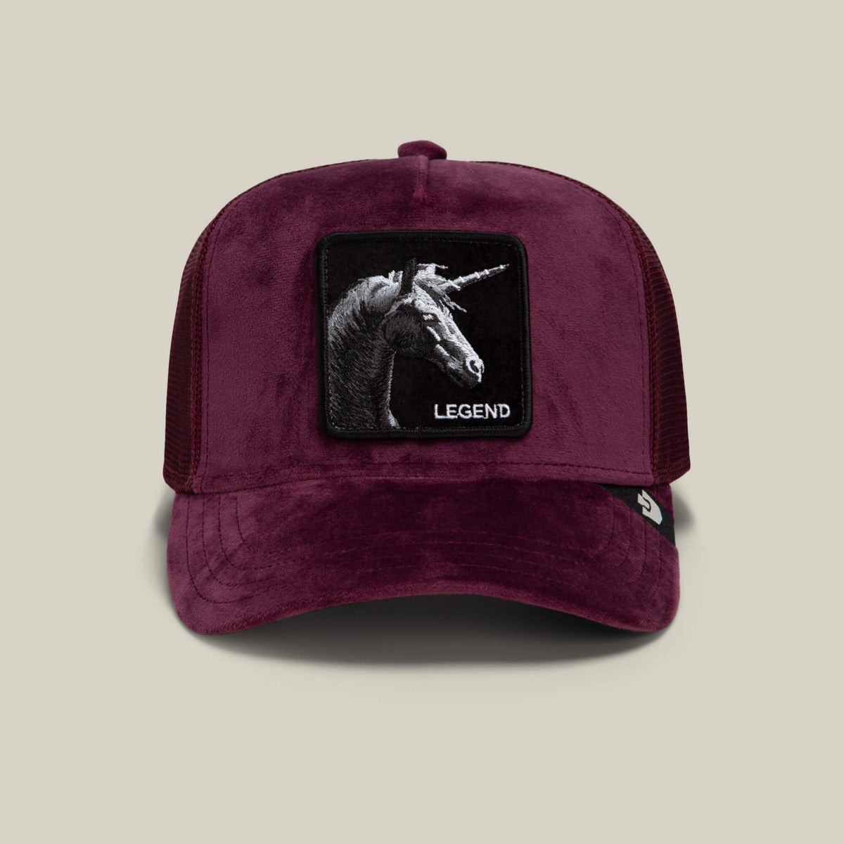 Goorin Bros. Velour Legend is a burgundy velour baseball cap in a classic trucker silhouette, featuring a mesh back and a striking patch with a black unicorn head and the word “LEGEND” embroidered beneath it.