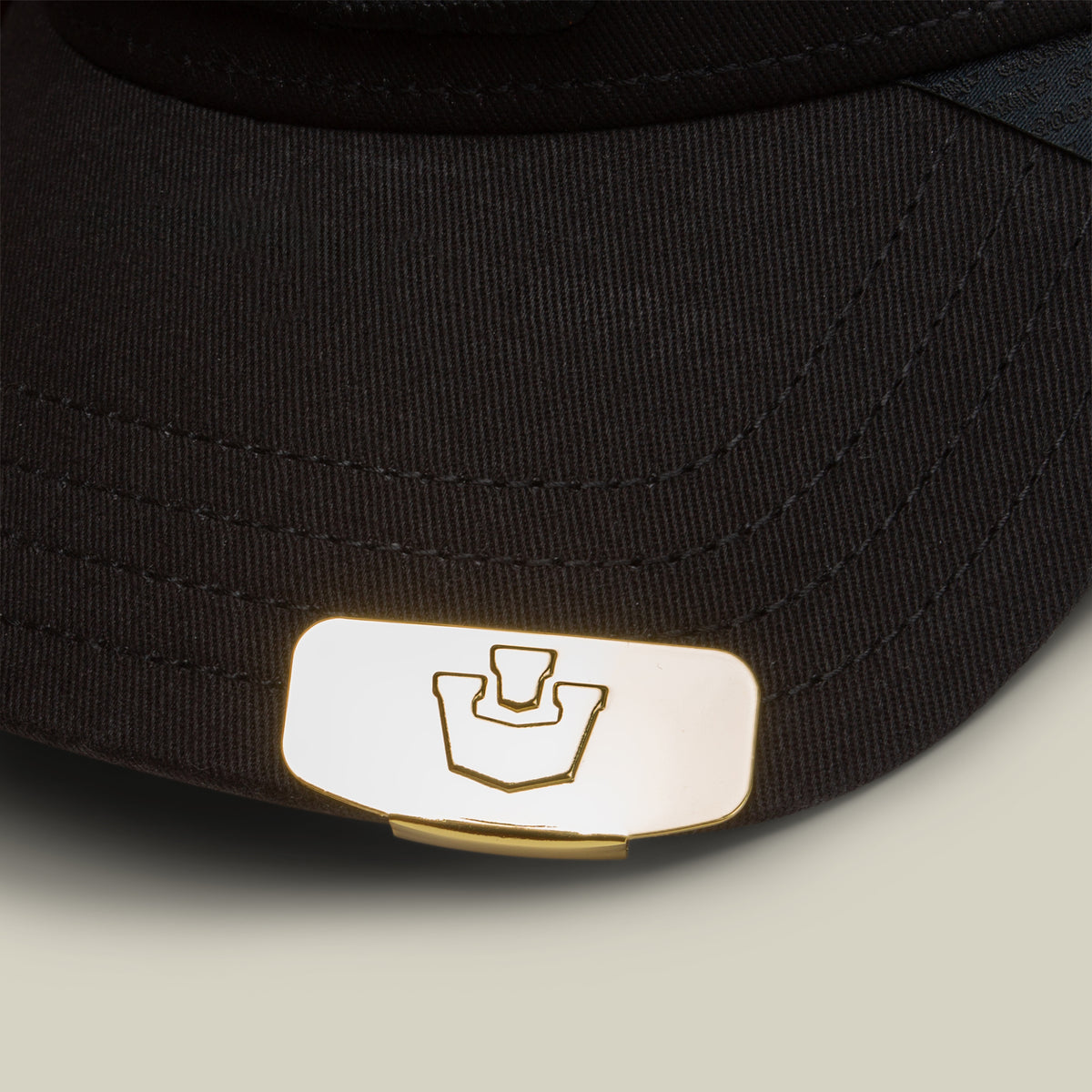 Close-up of the Goorin Bros. Castle CapLoc— a black hat accented with a gold zinc alloy metal emblem showcasing a stamped geometric logo on the brim, designed as a stylish accessory.