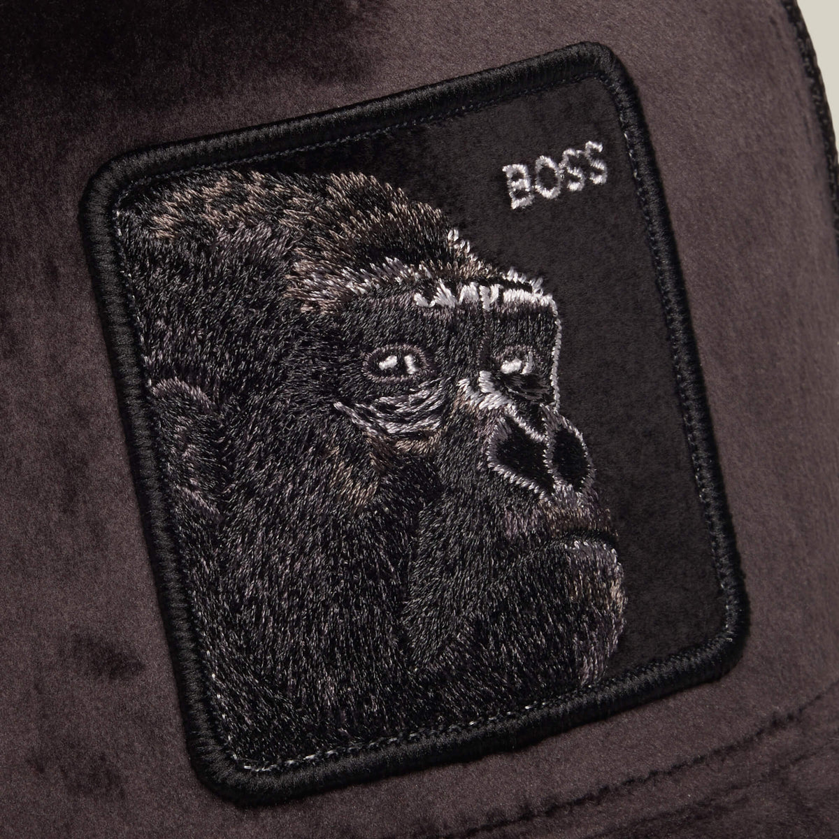 A black embroidered patch featuring a gorilla’s face and the word “BOSS” in white text is stitched onto a dark fabric background, creating a bold accent for any breathable mesh hat or polyester trucker—introducing the Velour Boss by Goorin Bros.