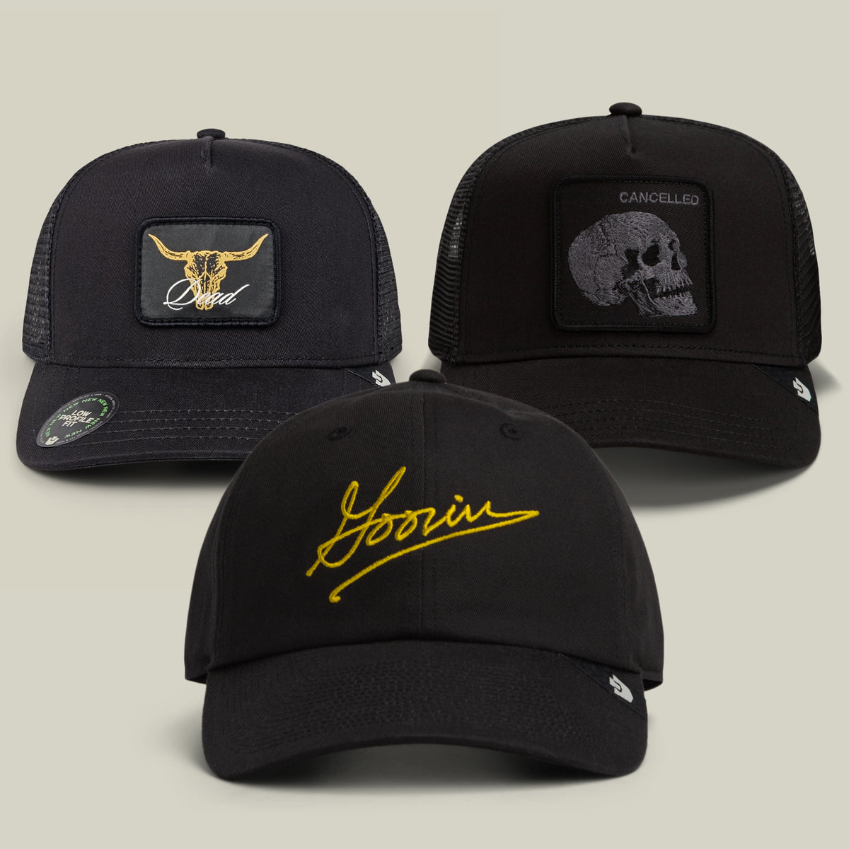 The Goorin Bros. All Black Every Shape Bundle features three black hats: one with a striking gold longhorn design, another with “Goorin” embroidered in yellow script, and a third adorned with a skull beneath the word “CANCELLED.”.