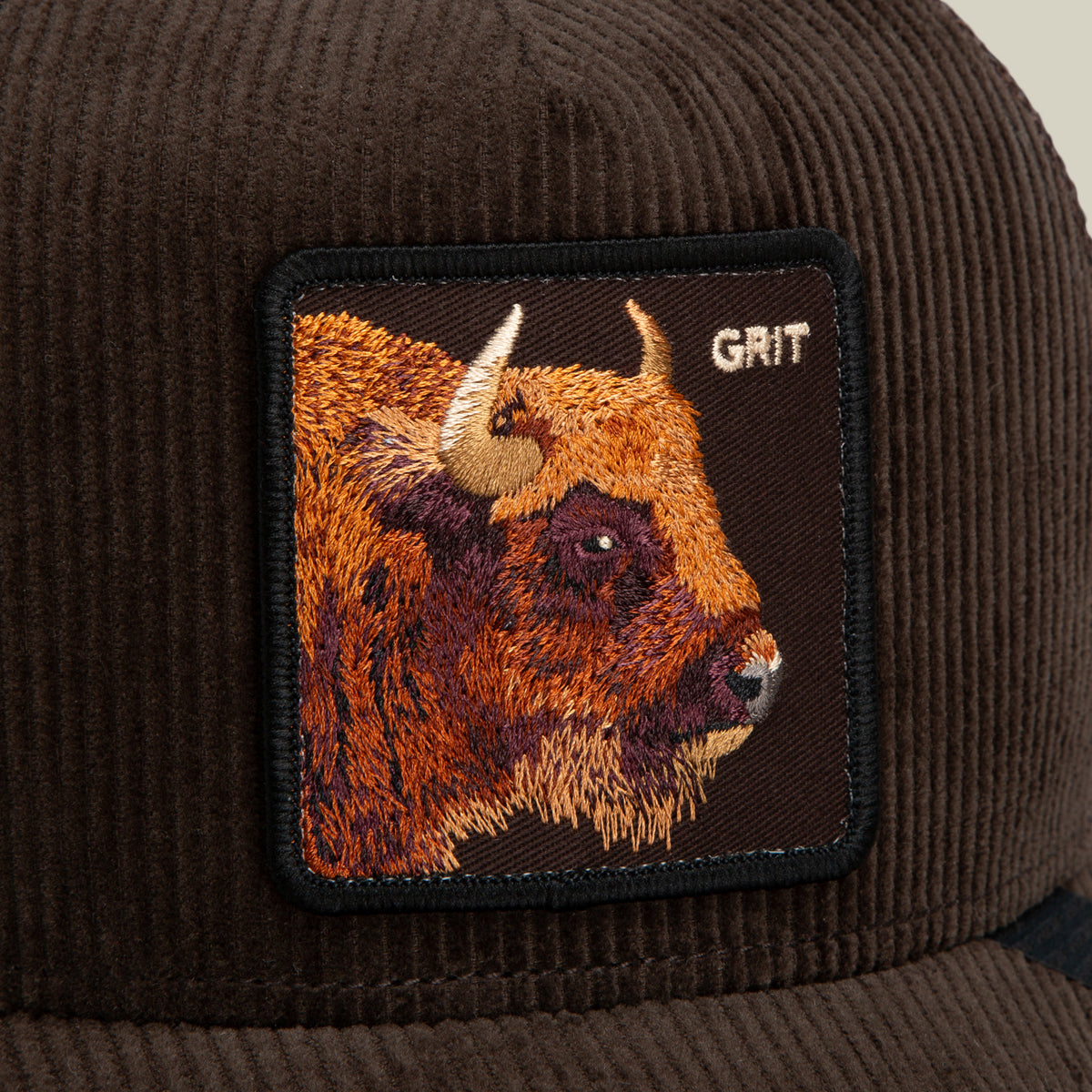 Close-up of the Corduroy Grit hat by Goorin Bros., showcasing its dark brown corduroy fabric, curved brim, and a rectangular patch with an embroidered bison and the word GRIT in the top right corner. Breathable mesh panels enhance comfort, making this accessory both stylish and rugged.