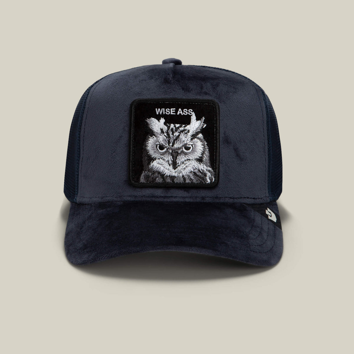 A dark blue Goorin Bros. “Velour Wise Ass” trucker hat featuring a patch with an owl and the words “WISE ASS” embroidered above it, displayed on a plain beige background.