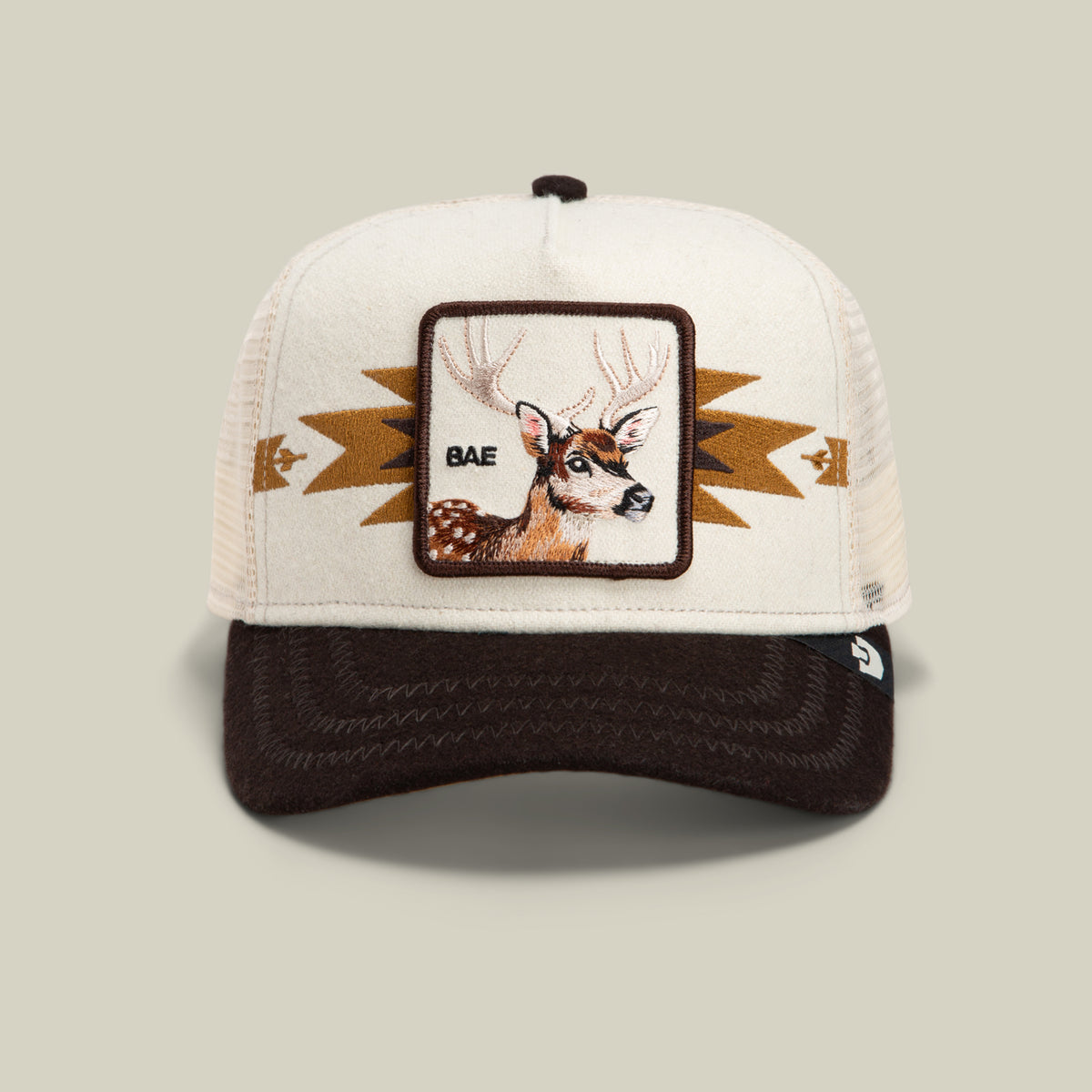 The Canyon Bae cap by Goorin Bros. is a beige and brown antler hat with a deer patch labeled “BAE” on the front, featuring geometric patterns on the sides; this premium blend mesh back cap combines style and comfort.
