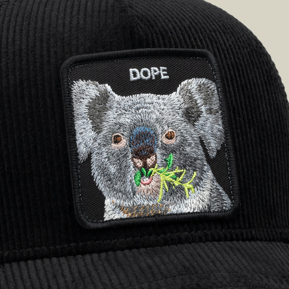 Close-up of the Goorin Bros. Corduroy Dope trucker hat in black, featuring an embroidered patch of a koala eating leaves with “DOPE” above its head.