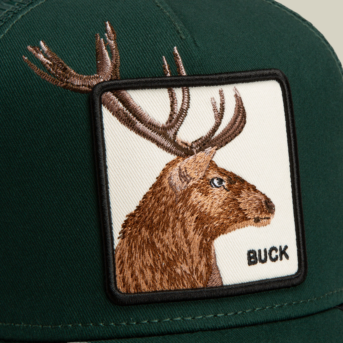 The Over the Line Buck by Goorin Bros. is a stylish green trucker hat featuring an embroidered patch of a brown buck’s head with antlers, along with the word “BUCK” stitched in black on the lower right corner of the patch. Crafted from a durable polyester-cotton blend and designed with breathable mesh panels, this cap keeps you comfortable all day long.