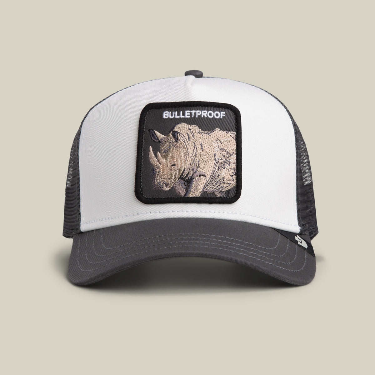 The Bulletproof Trucker by Goorin Bros. is a white and black mesh-back trucker hat featuring an embroidered front patch with a rhino and the word “BULLETPROOF.”.