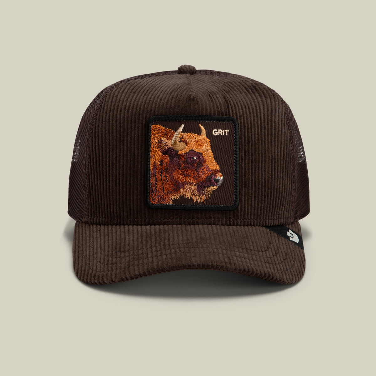 The Goorin Bros. Corduroy Grit trucker hat features dark brown corduroy fabric and a breathable mesh back, accented by a stitched patch showcasing a bison and the word “GRIT” on the front. It is finished with a curved brim for classic style.