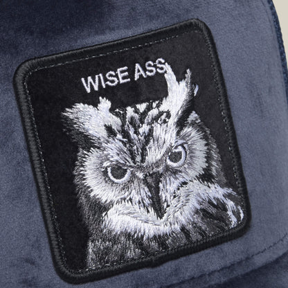 A close-up of the Goorin Bros. Velour Wise Ass hat on soft fabric, featuring an embroidered owl patch with the words “WISE ASS” above it.