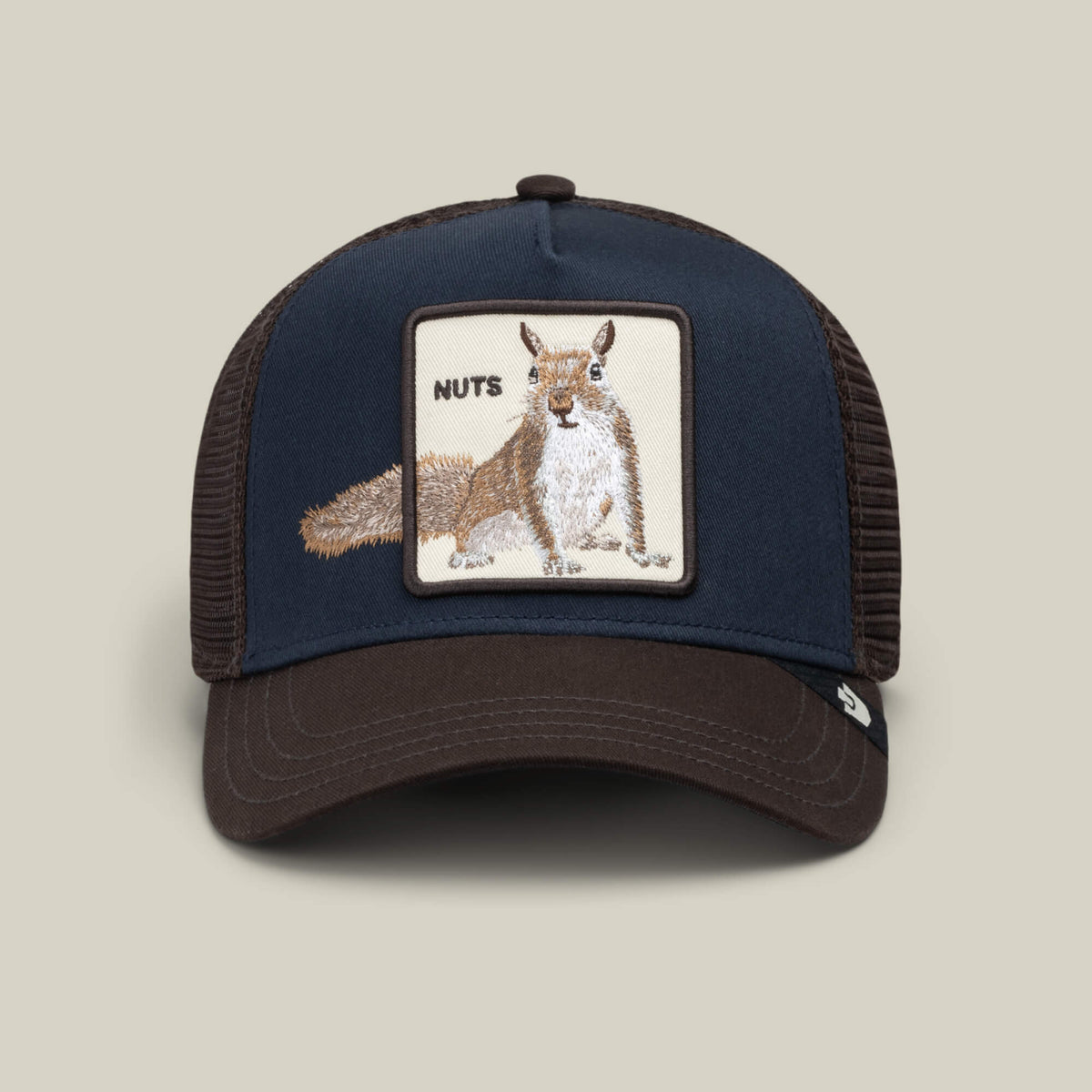 The Over the Line Squirrel trucker hat by Goorin Bros. features a navy and brown design with a mesh back, highlighted by an embroidered patch of a squirrel and the word “NUTS” on the front, making this playful accessory both stylish and fun.