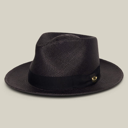 The Goorin Bros. John Sr. is a dark brown woven toquilla fedora with a wide brim, black ribbon band, and small gold pin, stylishly displayed on a light beige background for sun protection.