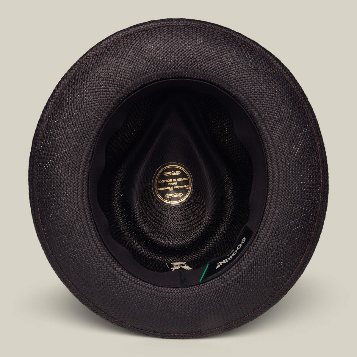 Top-down view of the inside of a black textured John Sr. teardrop fedora by Goorin Bros., featuring a gold label, black inner lining, and designed for 50 UPF sun protection.