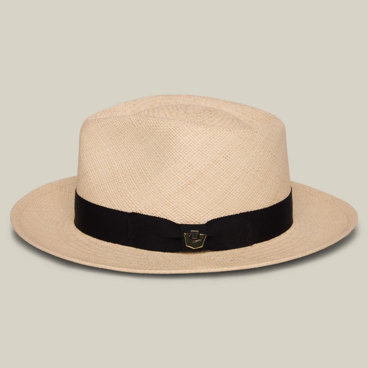 The Goorin Bros. John Sr. is a beige toquilla teardrop fedora with a wide brim, black ribbon band, small gold emblem on the front, and 50 UPF sun protection for stylish and safe wear.