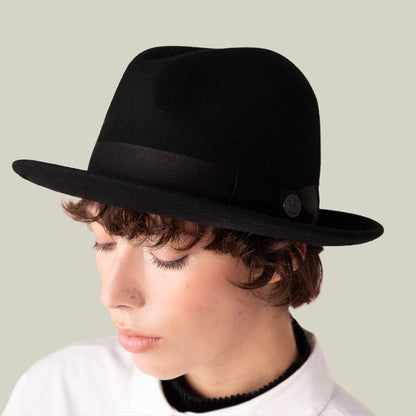 A person wears the Goorin Bros. "Dean the Butcher" fedora with a grosgrain hatband, eyes closed and looking down in a white collared shirt against a plain background.