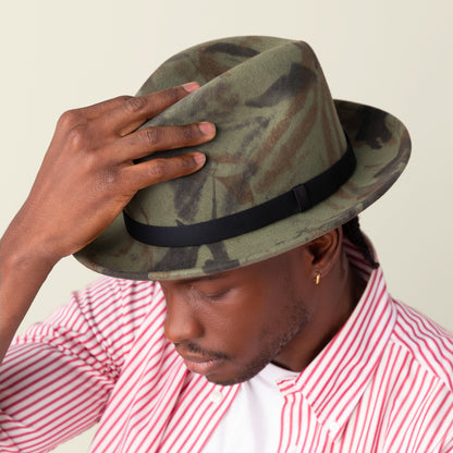 A man wearing the Goorin Bros. "Dean the Butcher" fedora with a grosgrain hatband and a red-and-white striped shirt looks down while holding the brim of his hat.